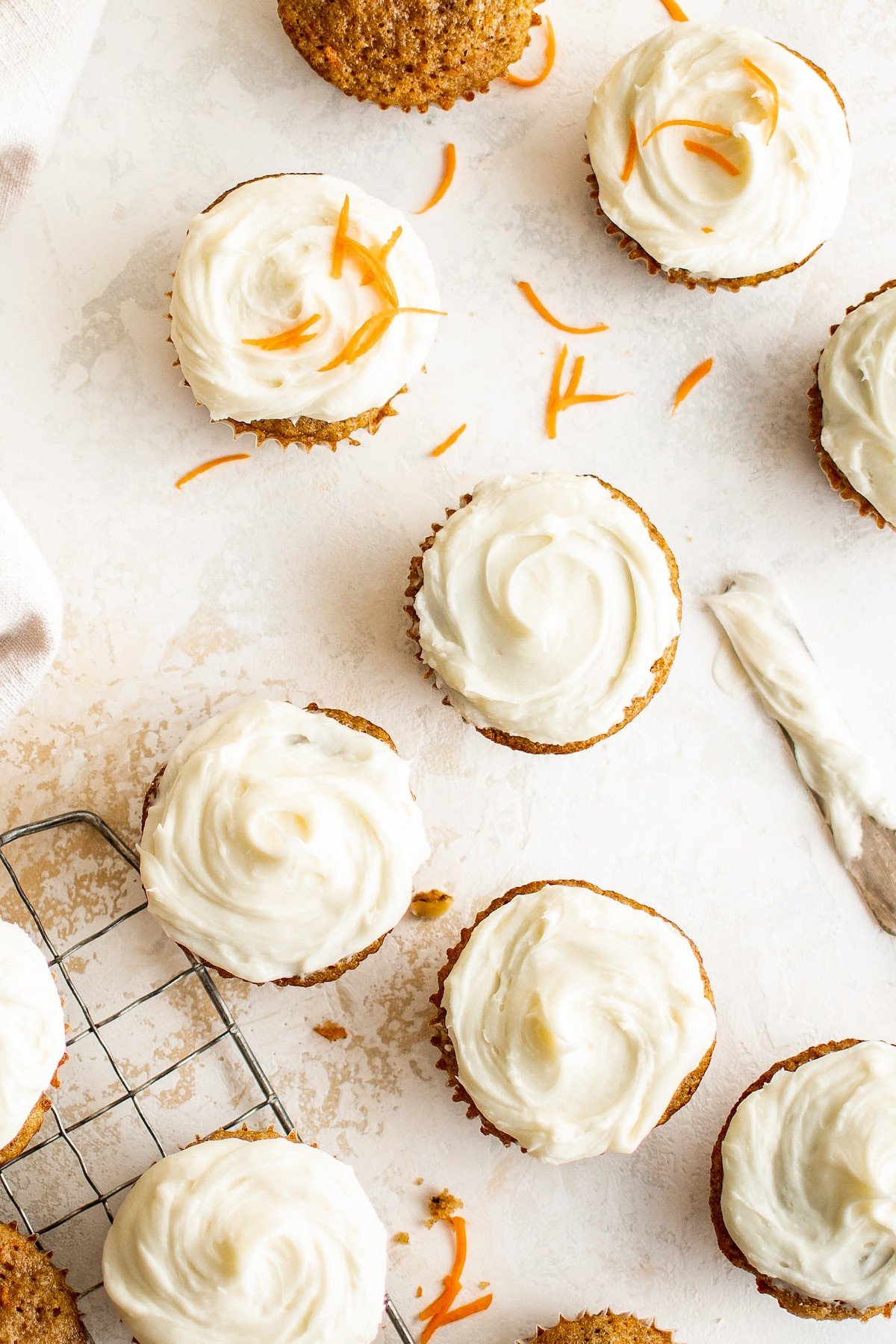 Frosted carrot cake cupcakes with grated shreds of carrot on top.