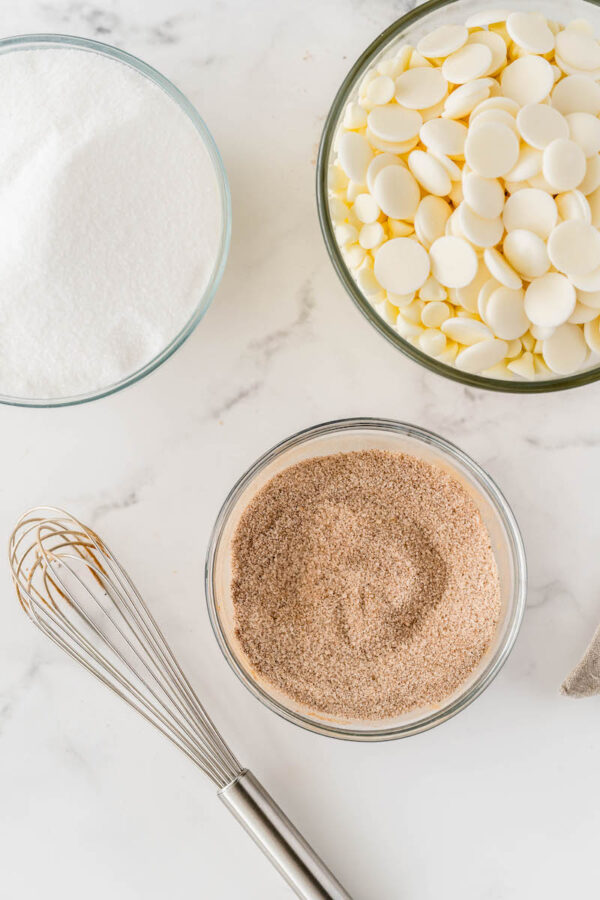 Cinnamon sugar in a glass bowl with a whisk and sugar and white chocolate in glass bowls.