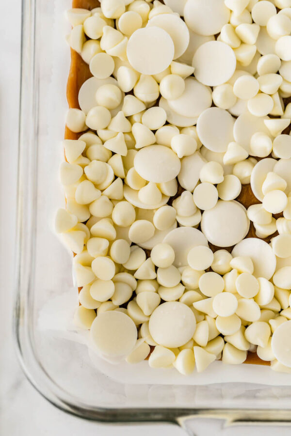 White chocolate chips sprinkled on top of candy in a baking dish.