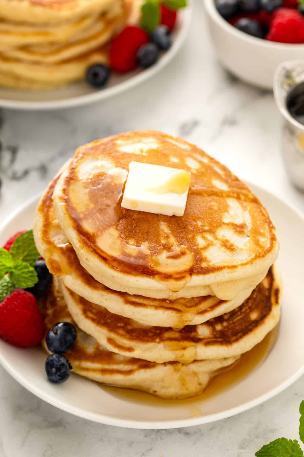 A stack of fluffy pancakes are topped with butter and syrup.