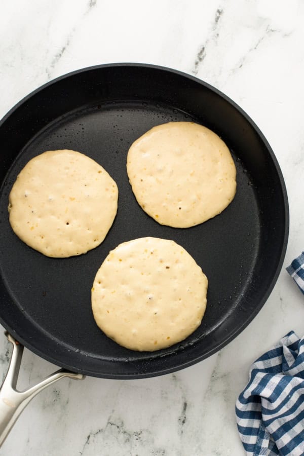 Three pancakes are cooking in a skillet.