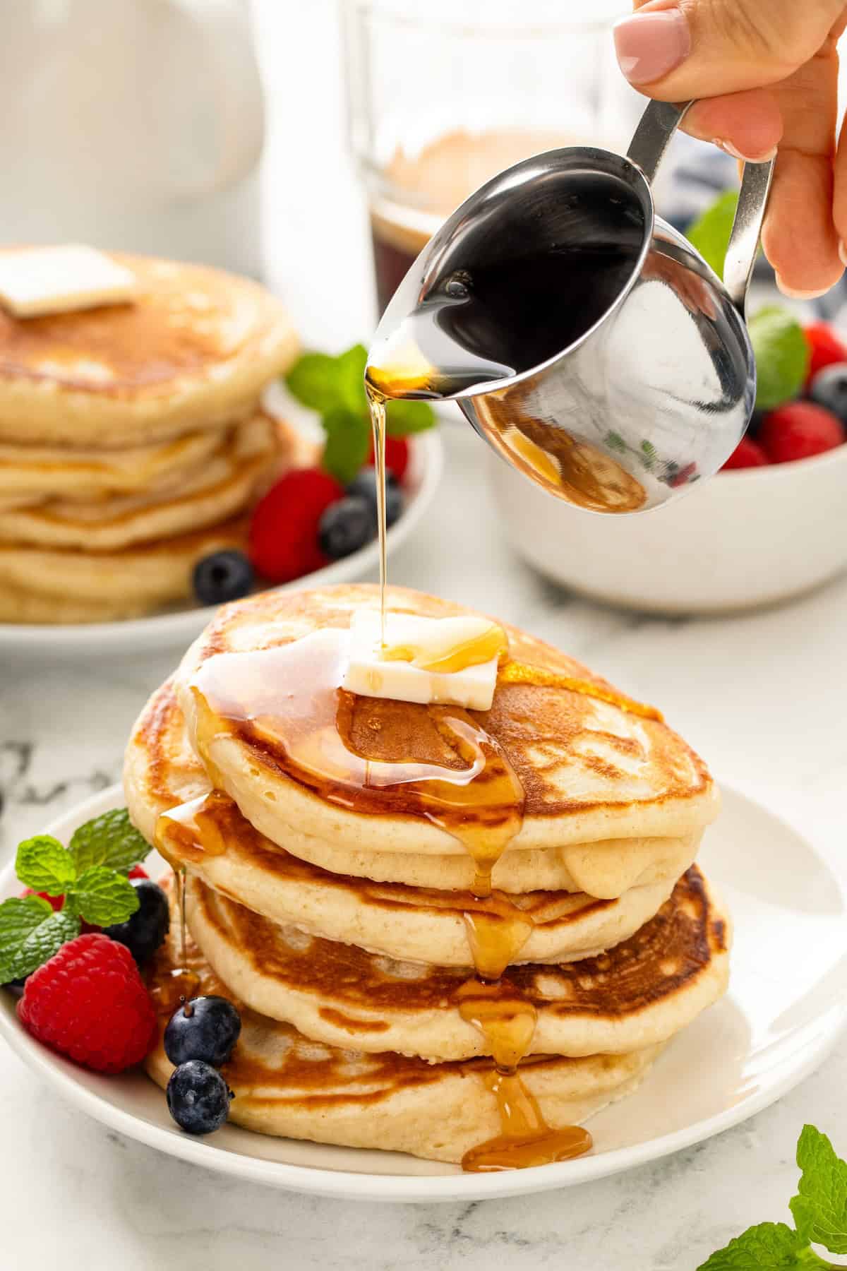 Syrup is being drizzled on top of a stack of homemade pancakes.