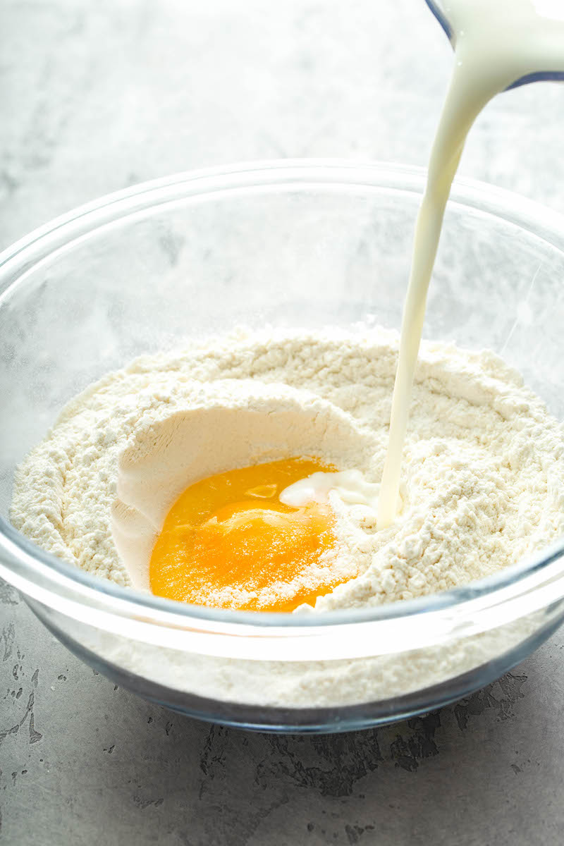 A bowl with flour, egg and milk being poured into it. 
