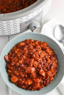 Pork and beans in a blue bowl with a crockpot and spoon in the back ground.