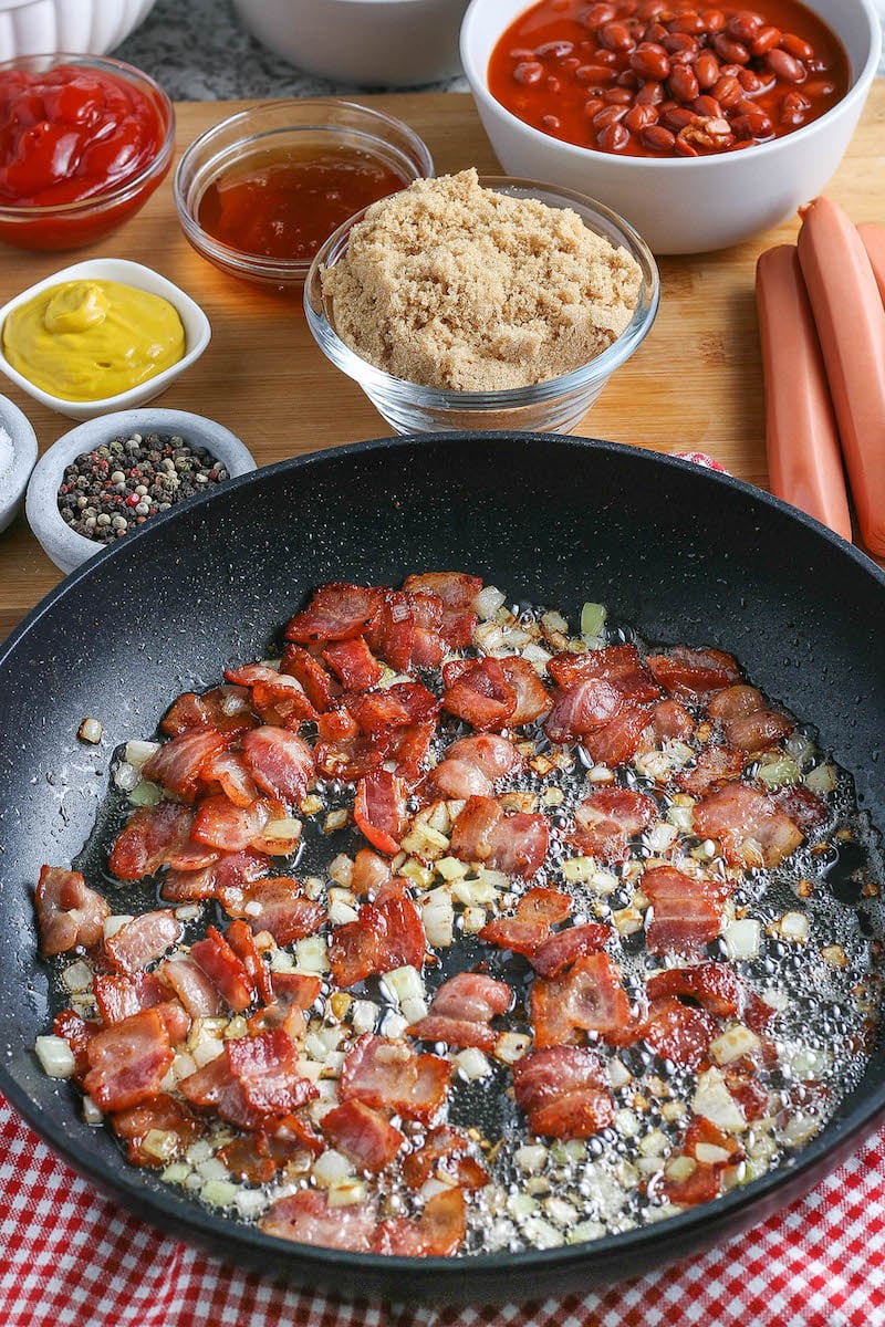 Bacon and onion fried in a skillet with other ingredients behind.