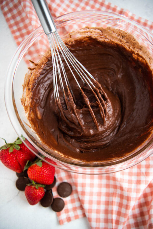 Brownie batter in a bowl with a whisk on a tea towel.