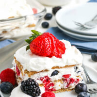 Slice of icebox cake with a sliced strawberry on top and more berries on the plate.