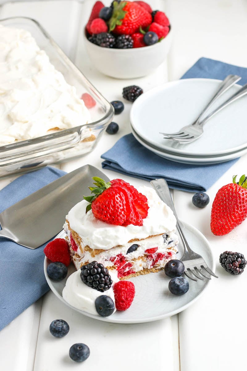 Slice of icebox cake on a plate with berries and a slice strawberry, and a fork next to it.