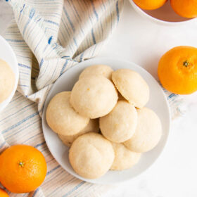 whipped shortbread cookies on a plate with oranges and a napkin besides them.