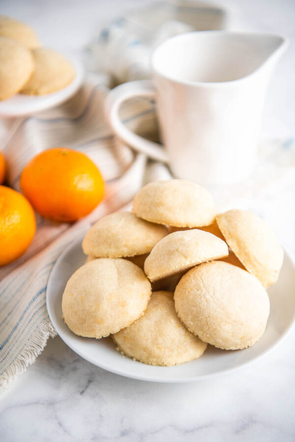 Shortbread cookies on a white plate with oranges and a pitcher of milk in the background.