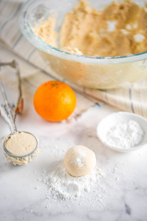 Shortbread dough rolled into a ball with dough in a bowl behind with a cookie scoop.