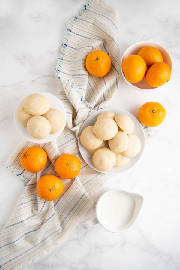 Overhead shot of whipped shortbread cookies on plates with oranges, milk and a tea towel. 