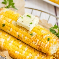 3 corn cobs with a pad of butter in a basket with parchment paper.