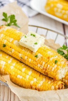 3 corn cobs with a pad of butter in a basket with parchment paper.