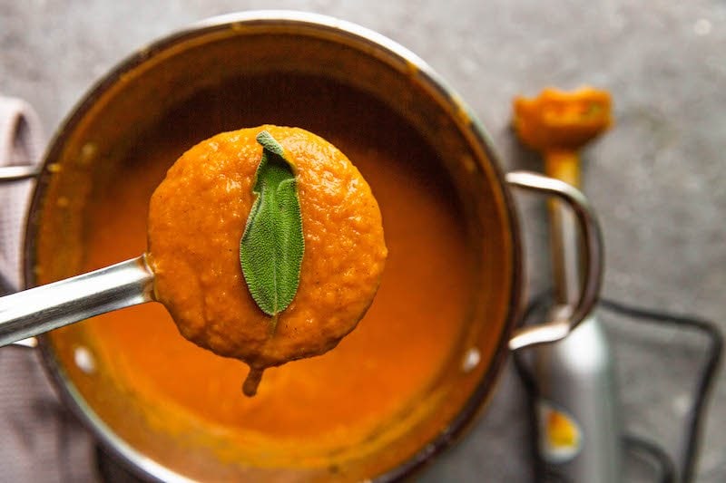 Pureed butternut squash soup in a ladle over a dutch oven