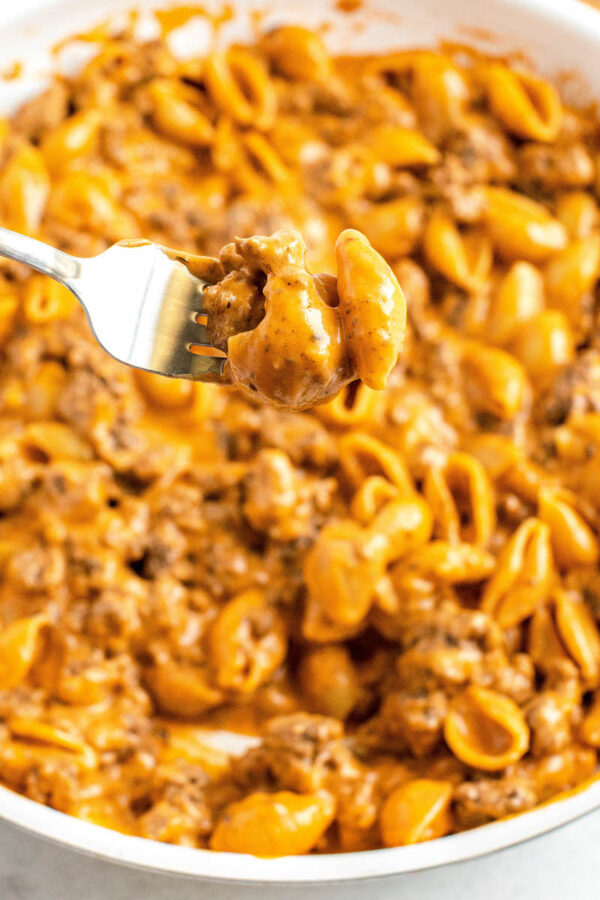 Cheeseburger pasta on a fork over a skillet filled with pasta.