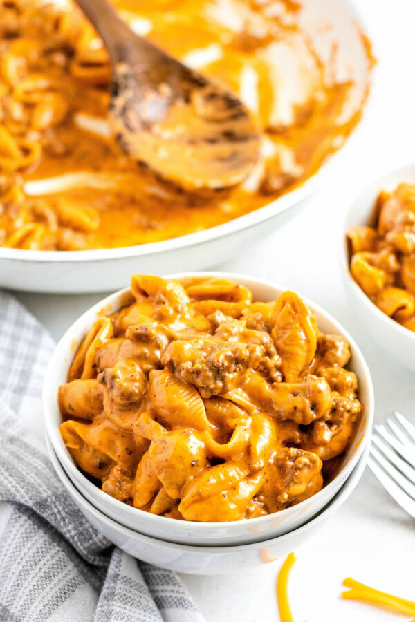 Homemade hamburger helper in a bowl with a napkin and a skillet with a spoon in the background.