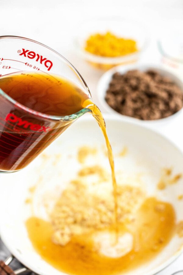 Beef broth being added to a skillet with garlic.