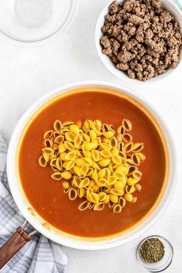 Pasta shells in tomato based sauce in a skillet with ground beef next to it in a bowl.