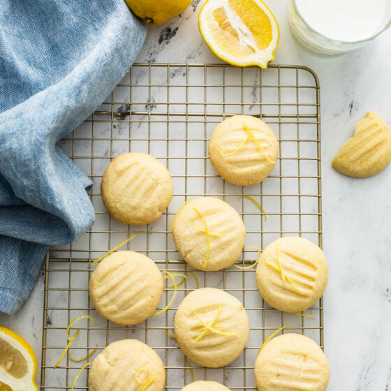 Overhead view of whipped shortbread cookies on a cookie sheet with a tea towel and lemons.