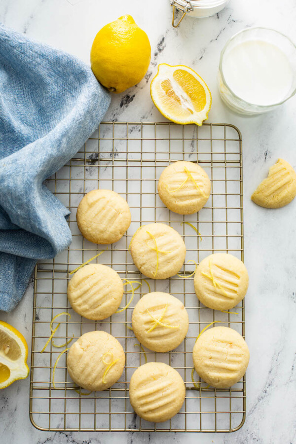 Overhead view of whipped shortbread cookies on a cookie sheet with a tea towel and lemons.
