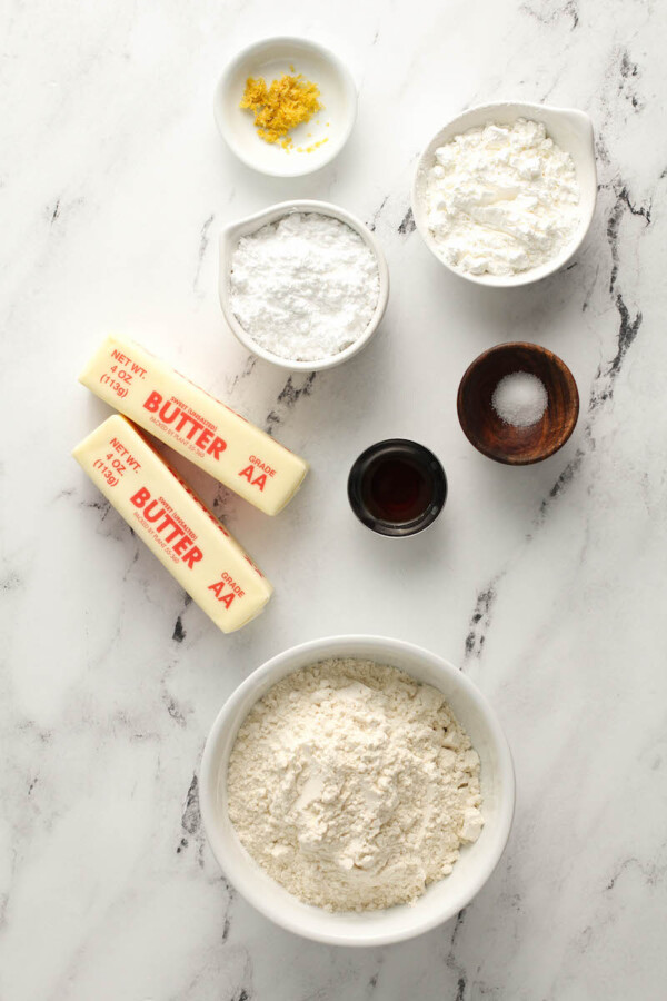 Ingredients for shortbread cookies in bowls on a marble countertop.