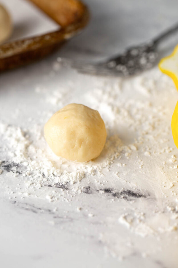 Shortbread cookie dough balls with cornstarch on a marble countertop.