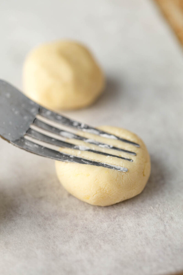 Shortbread cookie dough in a ball being flattened with a fork.