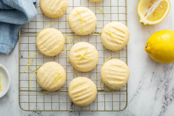 Overhead image of lemon whipped shortbread cookies on a cookie sheet with lemons and a blue tea towel.