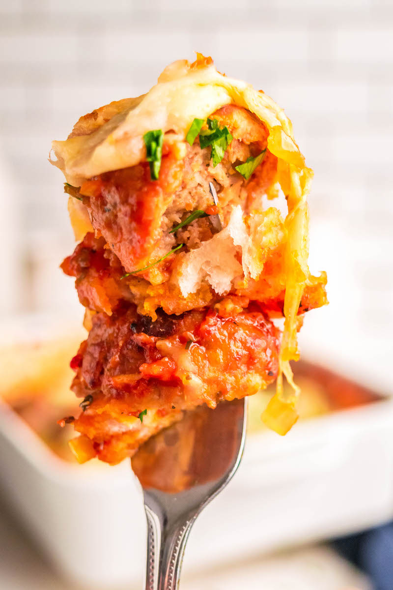 Fork full of baked meatball sub casserole, with pan in the background.