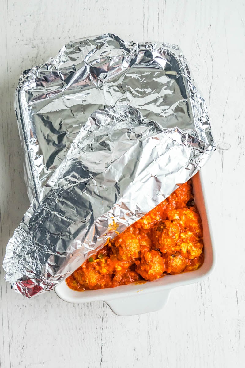 Pan of meatballs in marinara sauce, partially covered with aluminum foil.