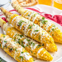 6 corn cobs on a plate with sour cream sauce, cotija cheese, and fresh cilantro.