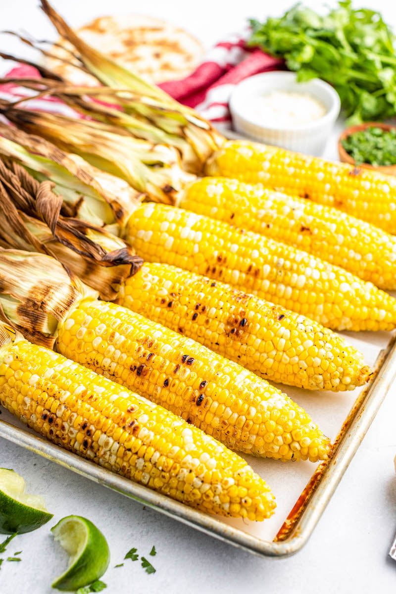 6 grilled corn cobs with the husks peeled back on a pan.