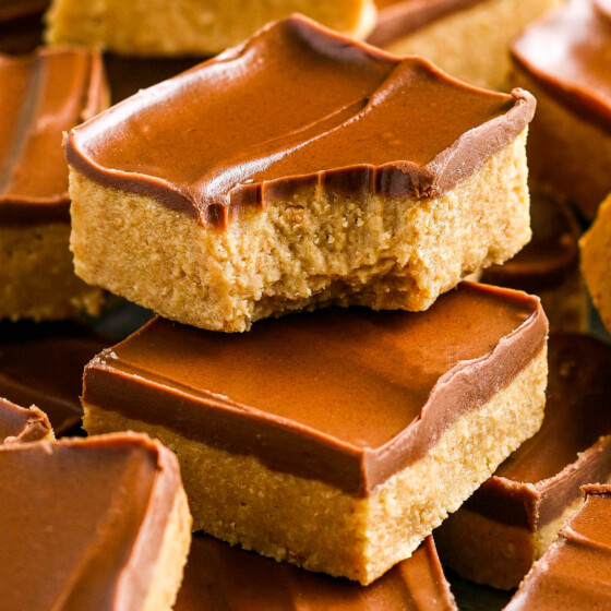 A stacked peanut butter bar with a layer of chocolate on top and a bite taken out of it.