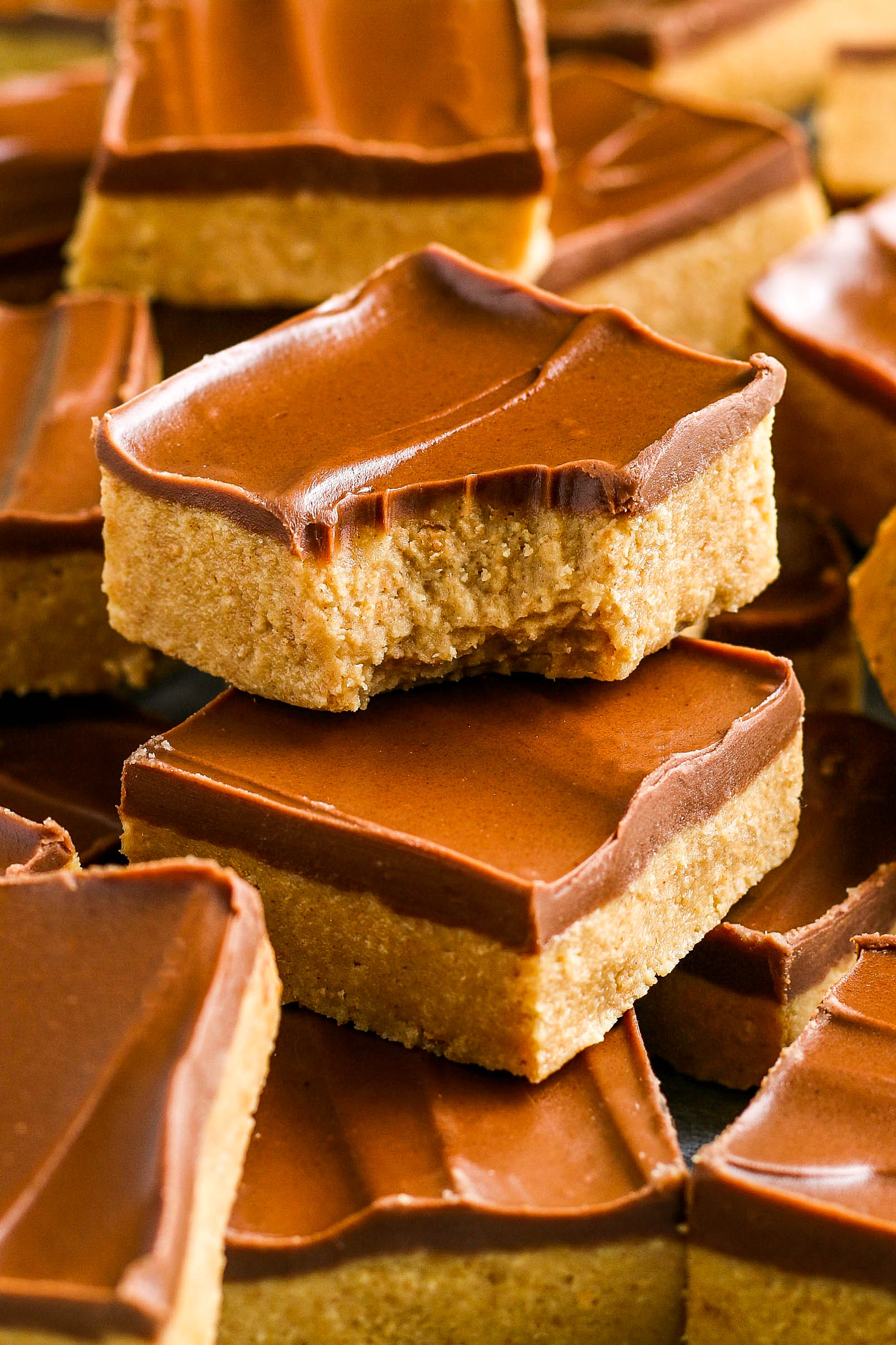 A stacked peanut butter bar with a layer of chocolate on top and a bite taken out of it.