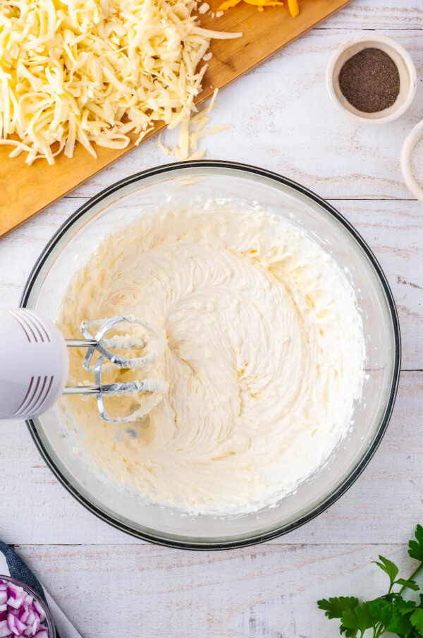 A bowl of beaten sour cream and cream cheese with the mixer in it.