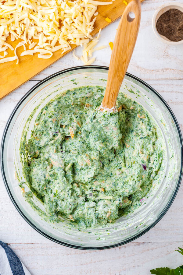 Mixed bowl of spinach dip with a wooden spoon in it.