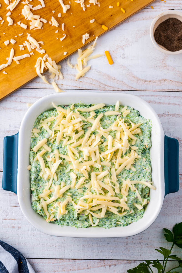 Spinach dip in a pan with shredded cheese on top.