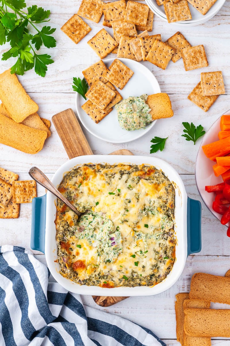 Baked spinach dip with a spoon in it, next to a plate of crackers.