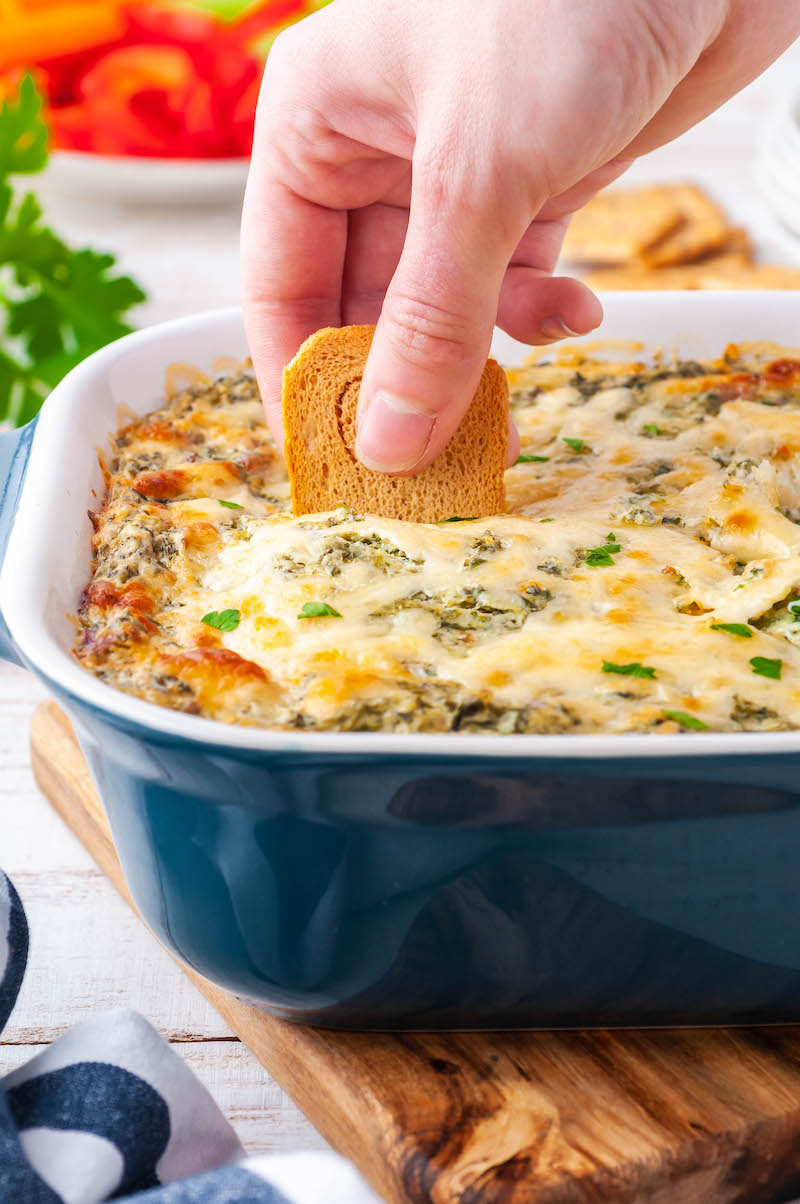 Baked spinach dip in a pan with a cracker in it.