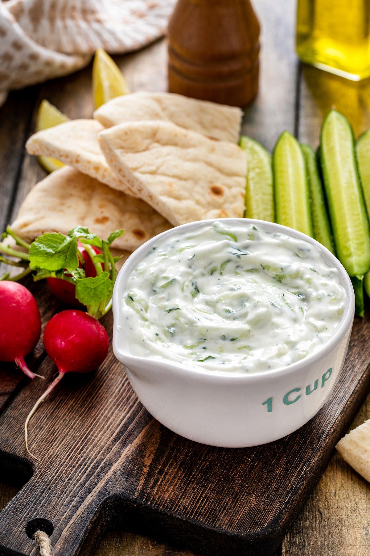 Bowl of Greek yogurt dip with pita bread, radishes, and cucumber wedges.