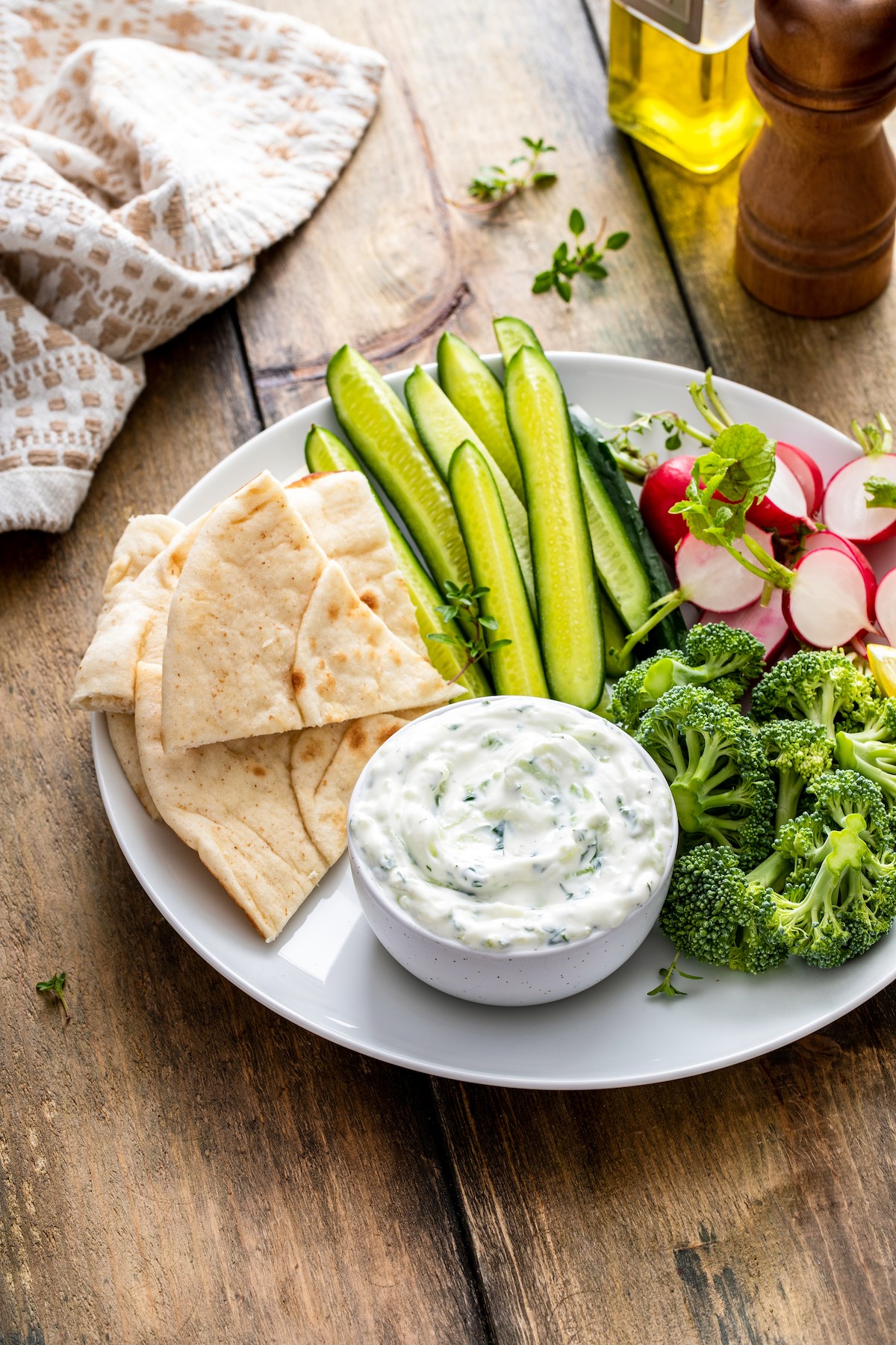 Tzatziki dip on a plate wit pita bread and cucumbers.