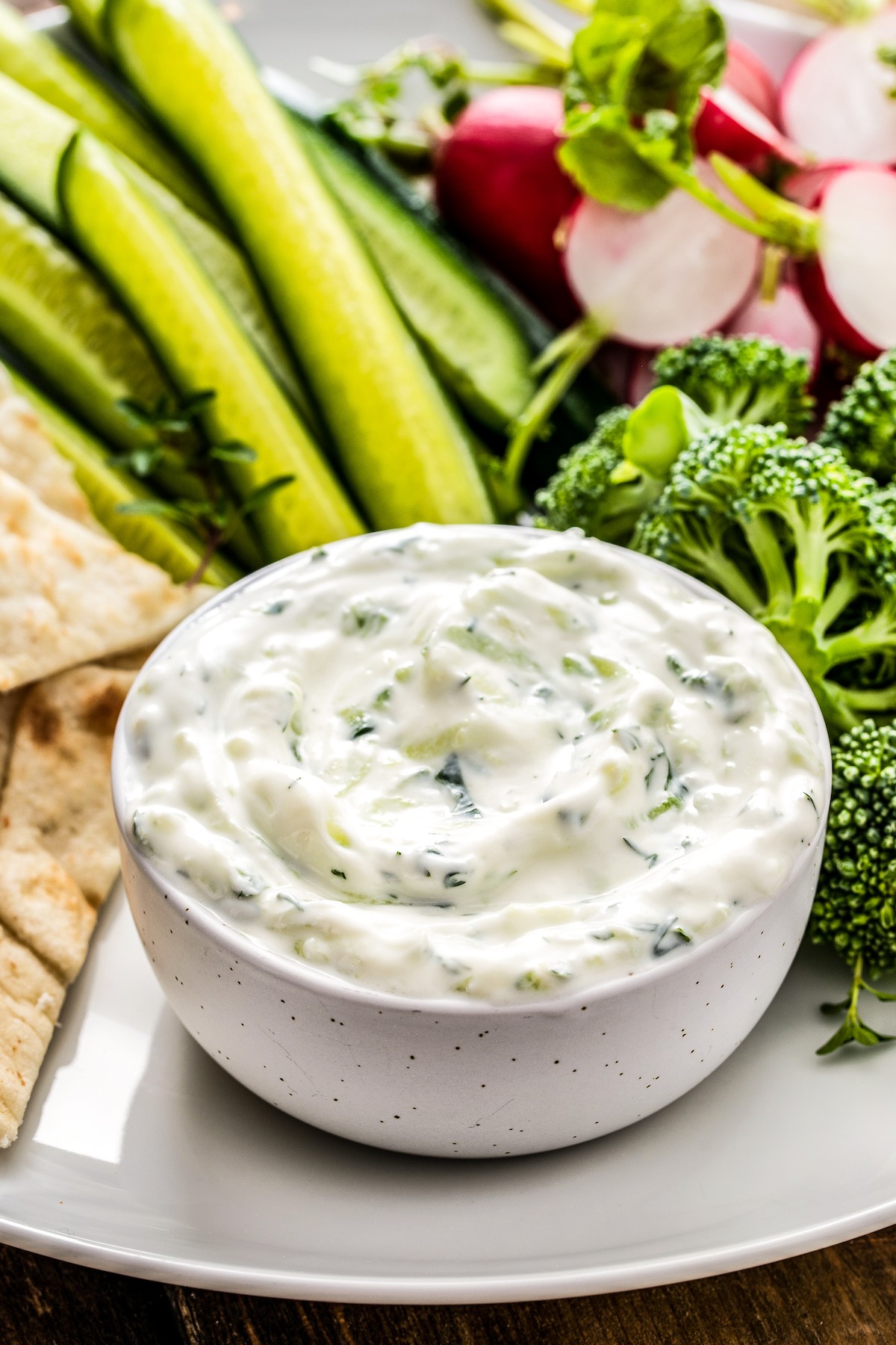 Bowl of cucumber dip with veggies on a plate.
