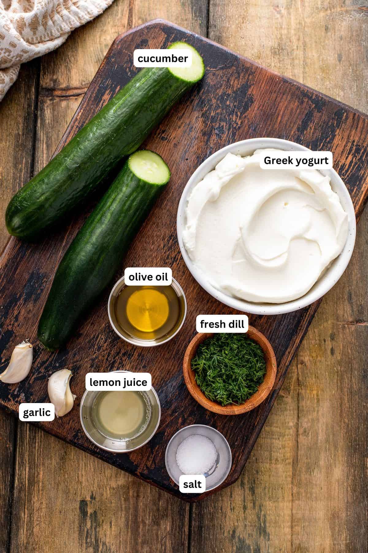 Ingredients for tzatziki sauce recipe arranged in bowls, listed from top to bottom: cucumber, greek yogurt, olive oil, fresh dill, garlic, lemon juice, salt.