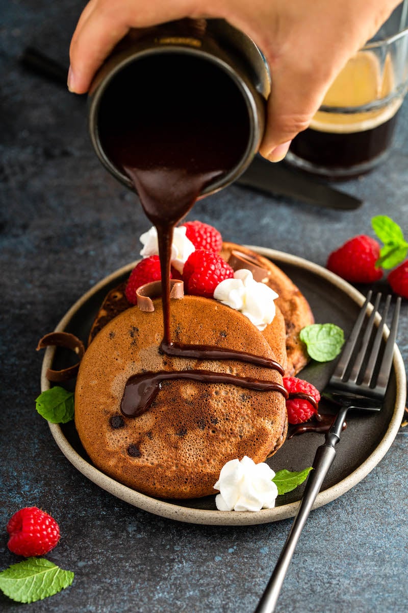 Chocolate sauce being drizzled over pancakes on a plate.