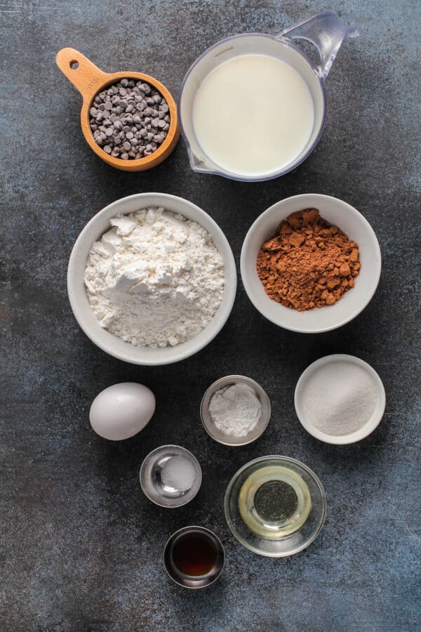 Overhead view of pancake ingredients in bowls on a dark board.