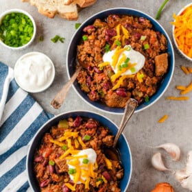 Two bowls of chili with cheese and sour cream on top.