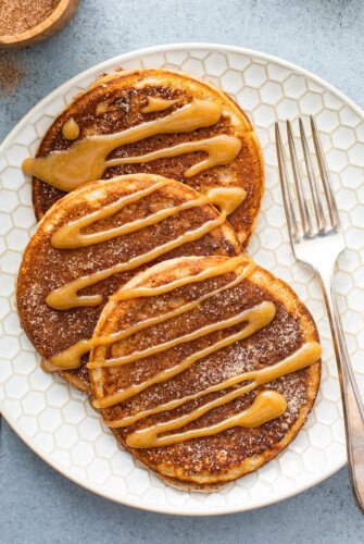 Up close image of churro pancakes on a white plate with a fork.