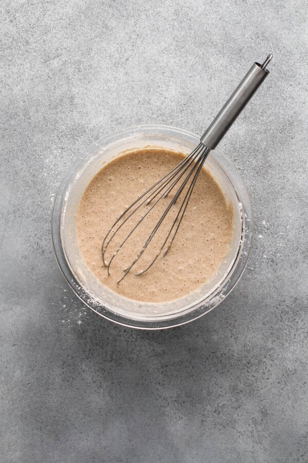 A bowl with pancake batter and a whisk inside it on a grey background.