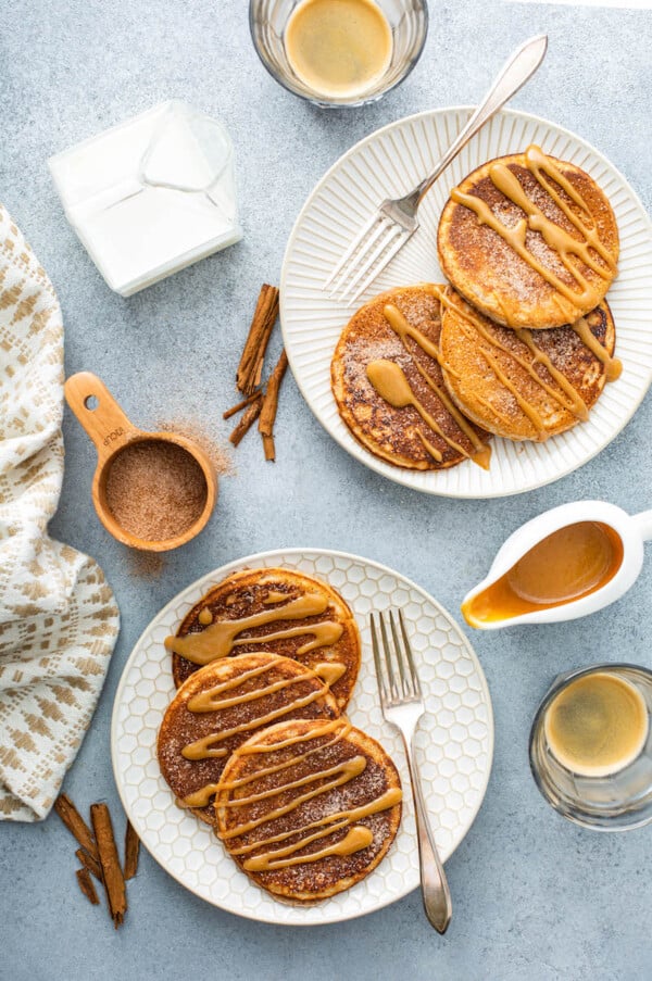 Two plates of pancakes with caramel drizzled on top.